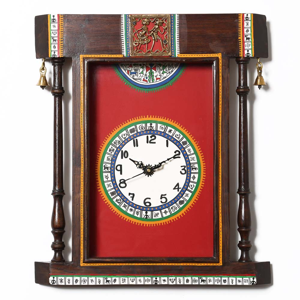 Handcrafted wooden wall clock with a vibrant red background, Indian folk art design, brass bell accents, and decorative wooden pillars.