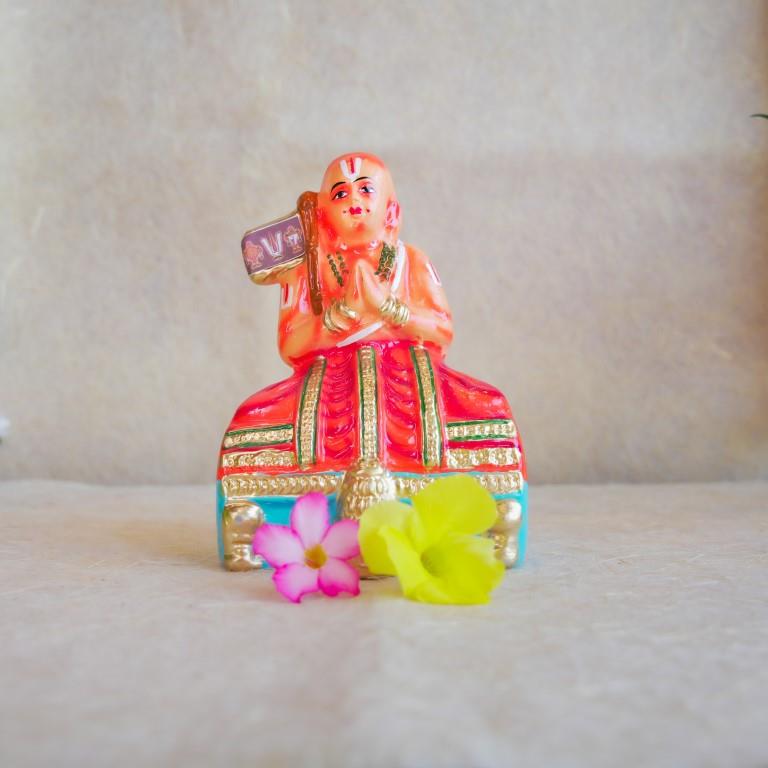 Hand-painted Navarathri Golu doll of Saint Ramanujar in a meditative pose, adorned in vibrant orange and gold attire.