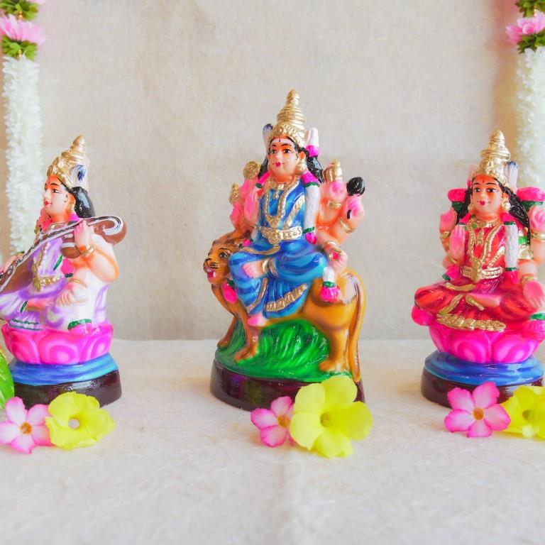 Handcrafted Navarathri Golu dolls of Durga, Lakshmi, and Saraswathi, beautifully painted and displayed with floral decorations.