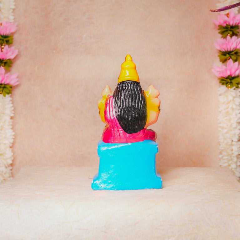 Hand-painted Navarathri Golu doll of Goddess Karumari Amman in a colorful seated posture with intricate detailing and vibrant pink and gold hues.