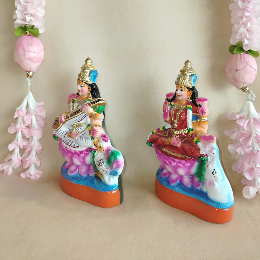 Handcrafted Lakshmi and Saraswathi Golu dolls set with vibrant colors, displayed with pink floral garlands.