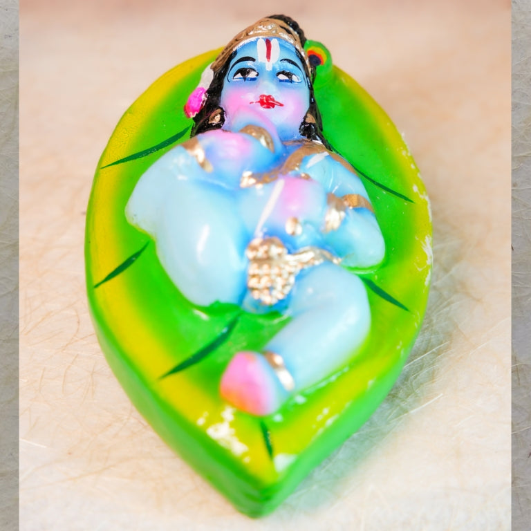 Handcrafted figurine of Baby Krishna lying on a green banyan leaf for Navarathri Golu decor.