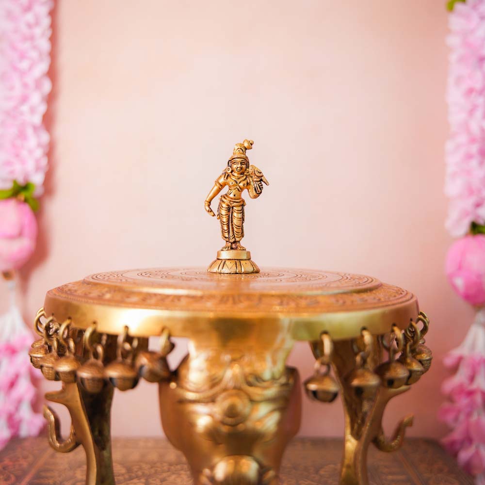 Small brass Andal idol with intricate detailing, displayed on a decorative pedestal.