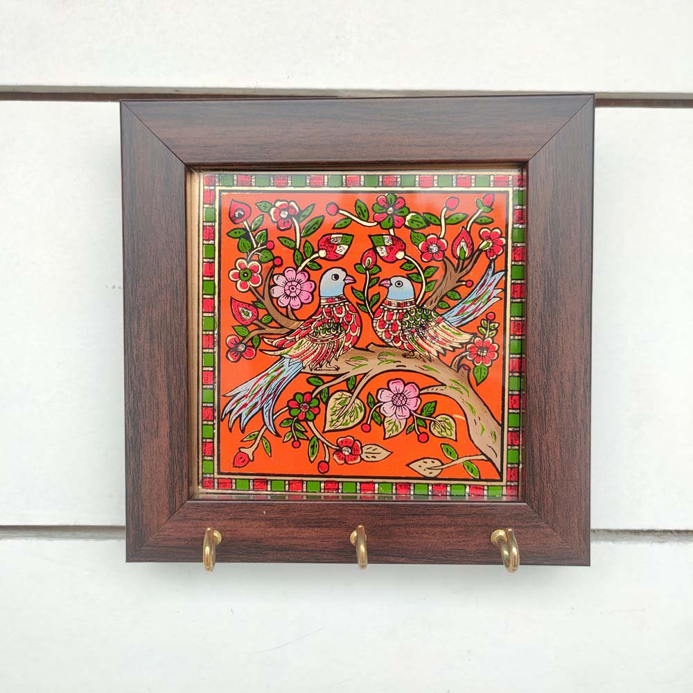 Decorative keyholder featuring a hand-painted motif of a pair of birds on a vibrant Red background, framed with dark wood, and equipped with key hooks.