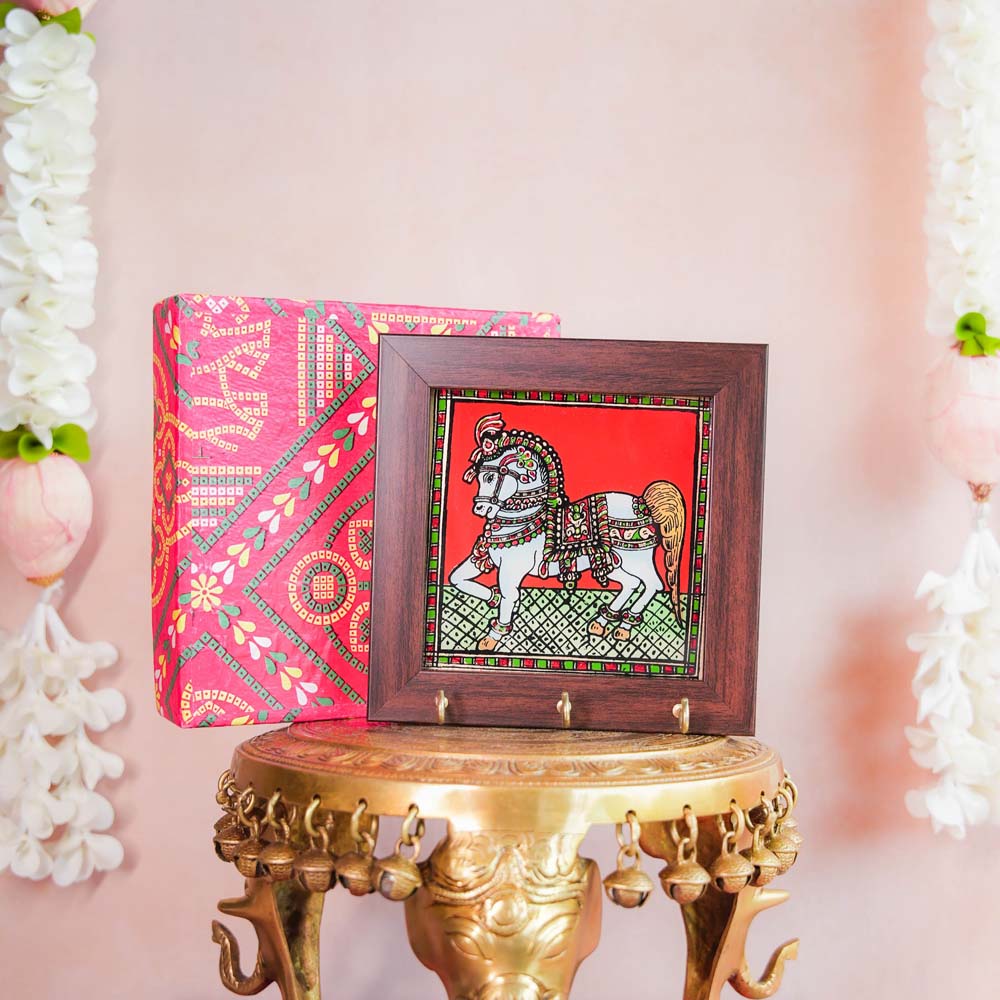 Decorative keyholder featuring a hand-painted Indian horse design on a vibrant Red background, framed with dark wood, and adorned with key hooks.