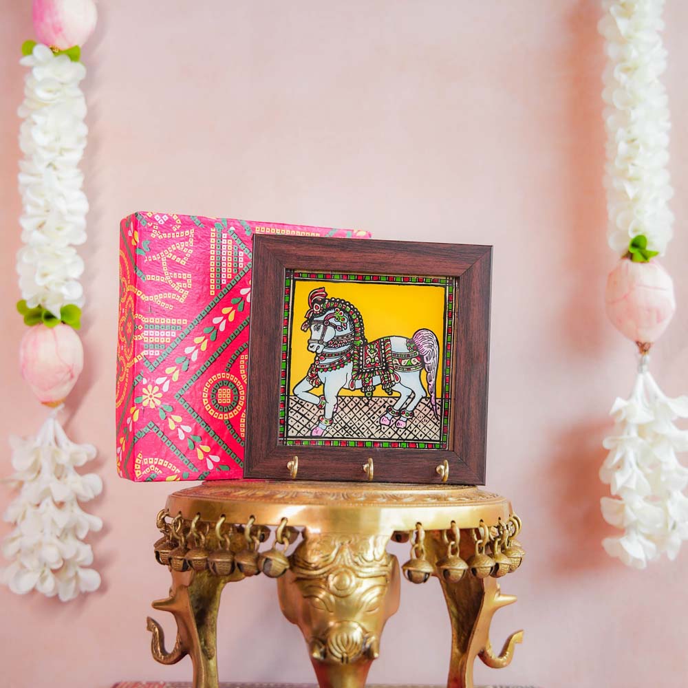 Decorative keyholder featuring a hand-painted Indian horse design on a vibrant yellow background, framed with dark wood, and adorned with key hooks.