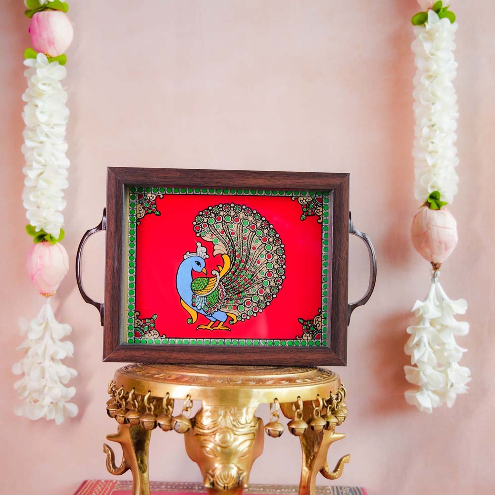 Decorative tray featuring a hand-painted Indian peacock design on a vibrant Red background, framed with dark wood and metallic handles, displayed on a traditional brass stand.