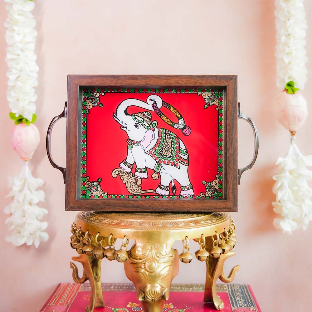 Decorative tray with a hand-painted blessing elephant motif on a vibrant Red background, framed with dark wood and metallic handles, displayed on a traditional brass stand.