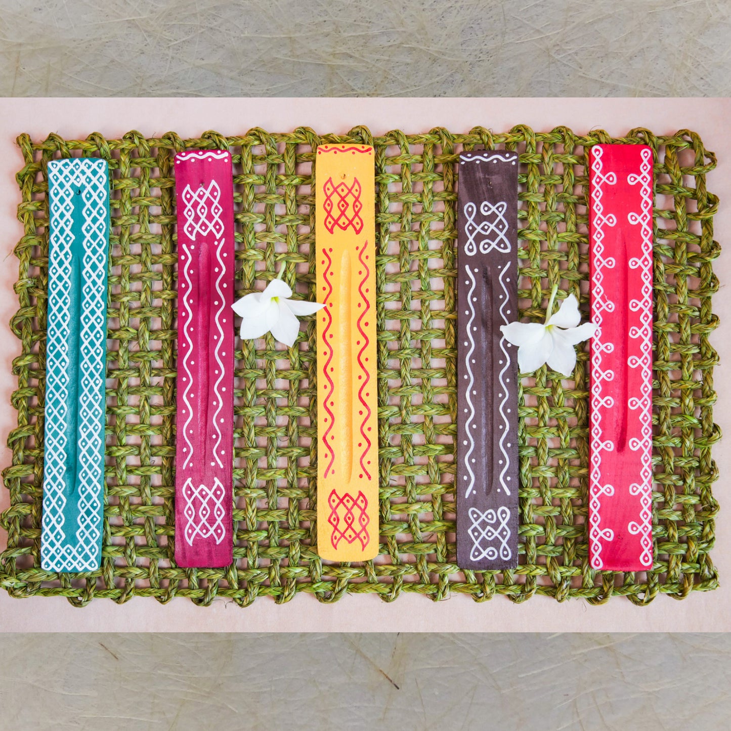 Handcrafted Kolam Incense Stick Holders with traditional Kollam art patterns, featuring vibrant colors on a woven green mat.