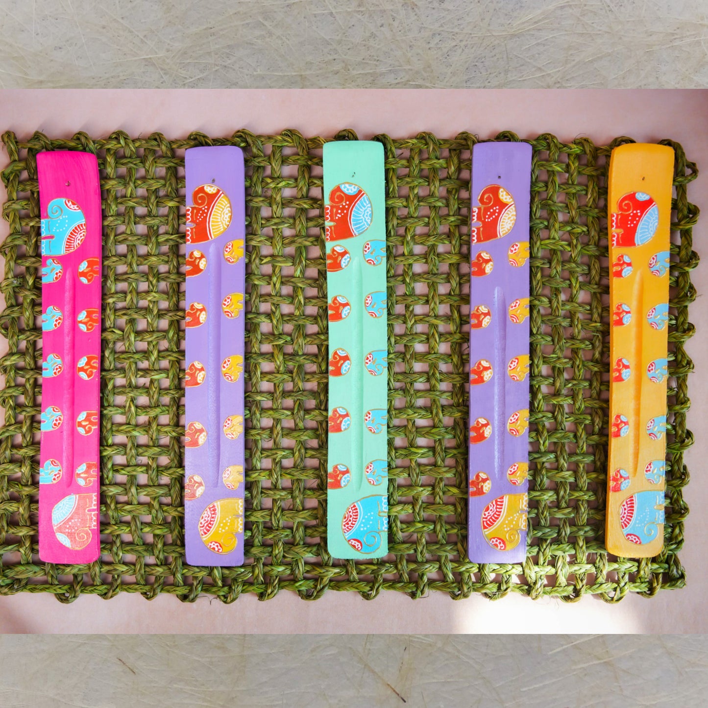 Handcrafted Elephant Incense Stick Holders with Madhubani art designs, featuring colorful elephant motifs on a woven green mat.