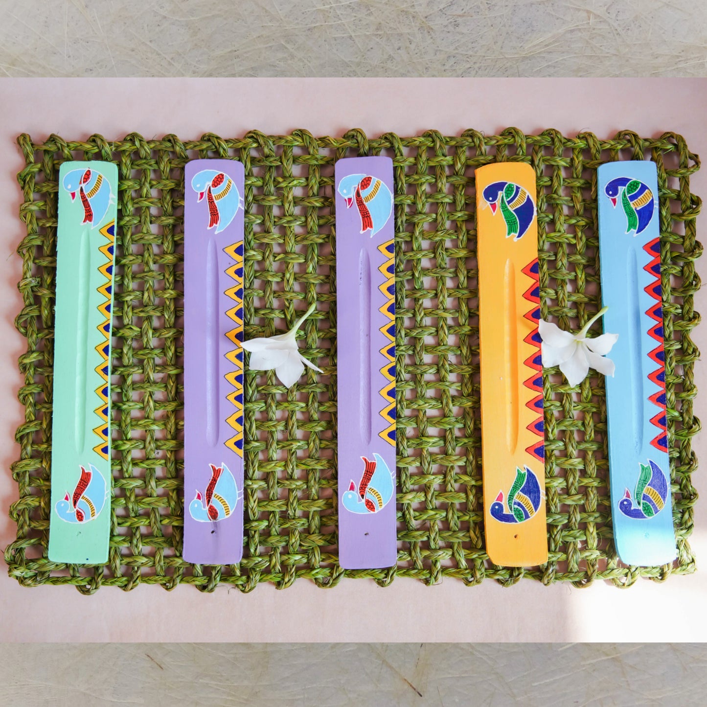Handcrafted Annam Incense Stick Holders with Madhubani art designs in assorted vibrant colors, featuring traditional bird motifs on a woven mat.