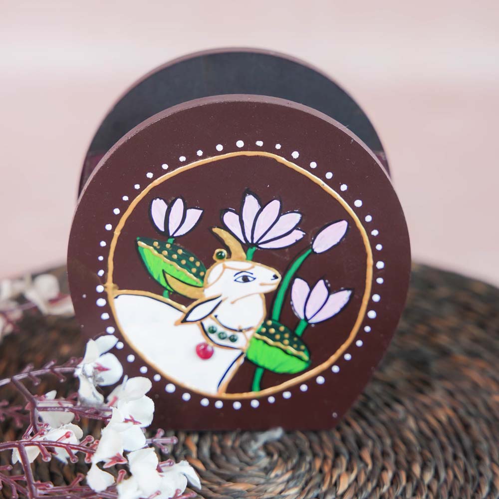 Hand-painted wooden penstand with a white cow design surrounded by lotus flowers, crafted on a brown background.