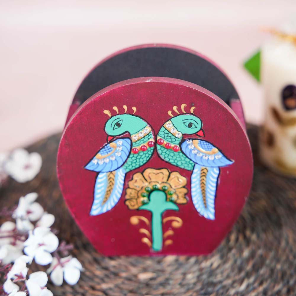Hand-painted wooden penstand with a design of two colorful parrots perched above a floral motif, placed on a woven mat with decorative floral accents.