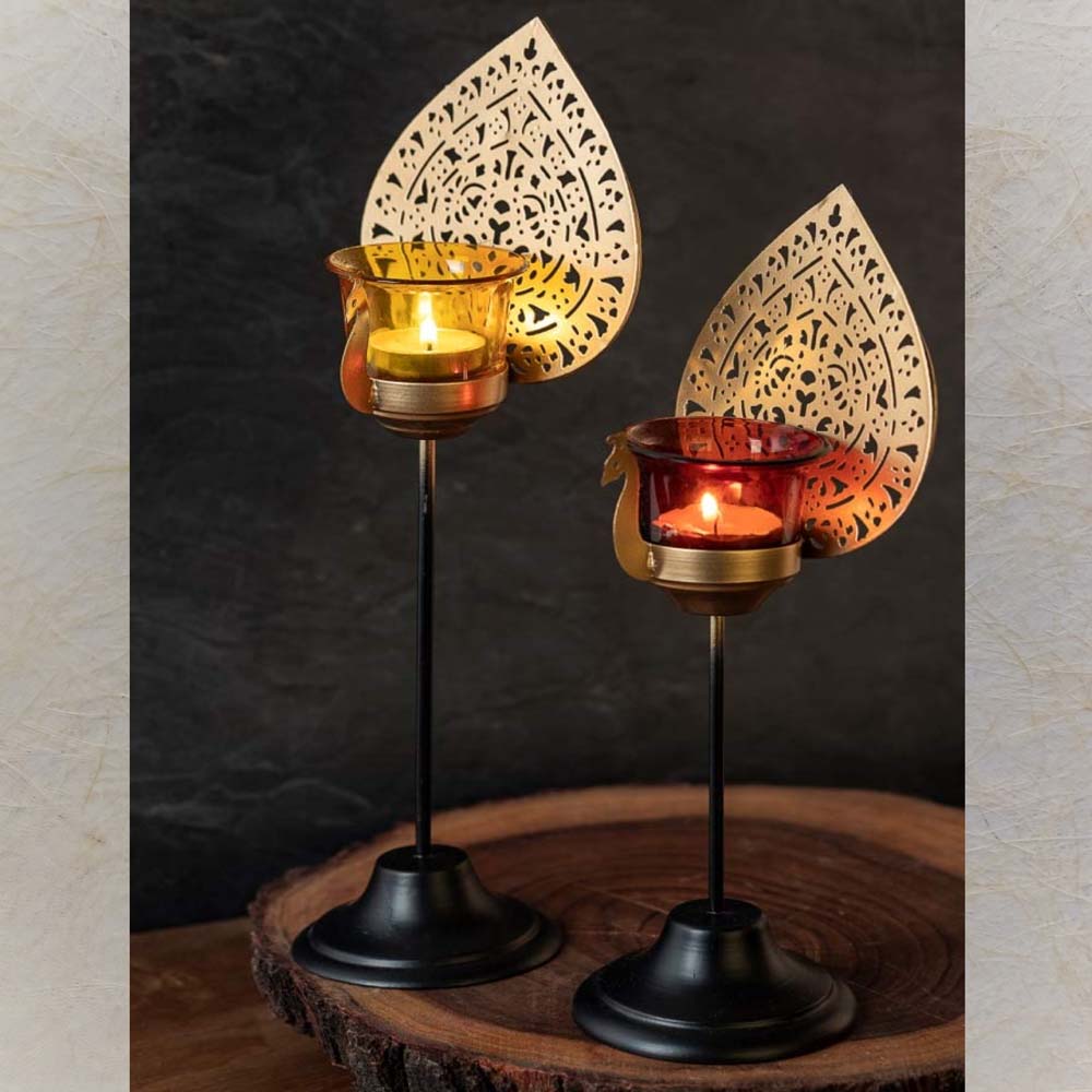 Lustre Peacock Candle Holder Set of 2 with perforated gold metal peacock tails and amber and ruby red glass votive cups, mounted on black metal stands.