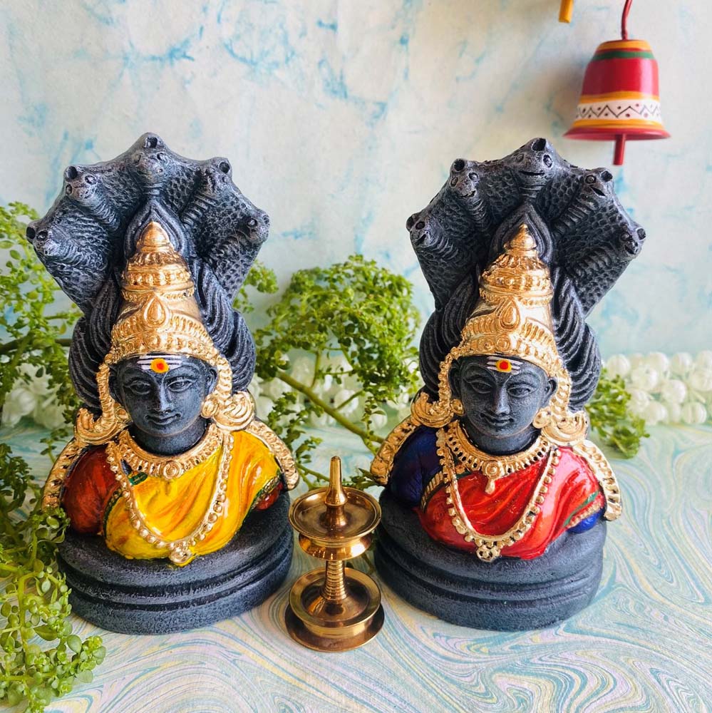 Two handcrafted Amman bust Golu dolls with a stone-like finish, featuring vibrant color accents in yellow and red, adorned with intricate details and a brass lamp centerpiece.