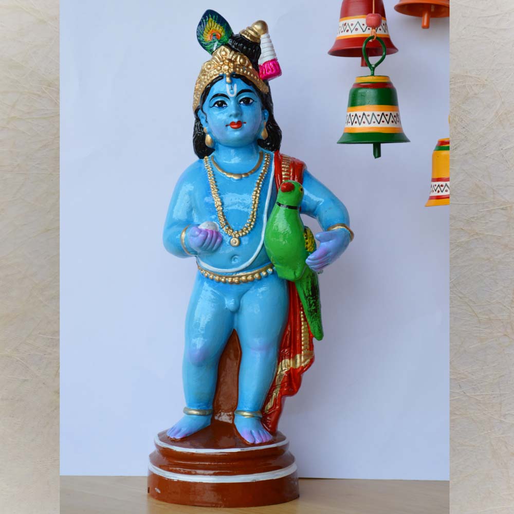 Handcrafted Golu doll of Lord Krishna holding a vibrant Parrot, adorned with intricate details and painted in vibrant blue, green, and gold tones.