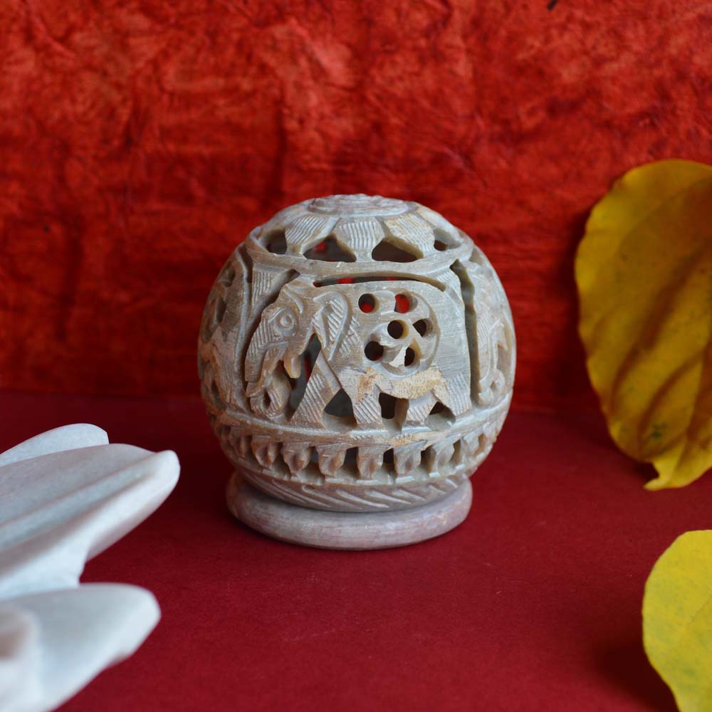 Hand-carved Marble Galaxy Filigree Ball T-Light Holder with intricate elephant patterns, glowing warmly.