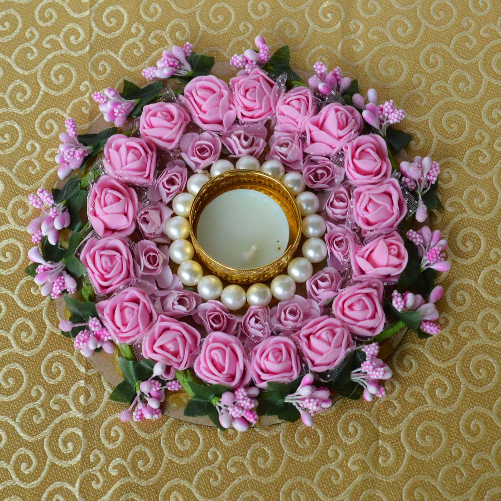 Round T-light diya decorated with pink artificial roses, pearls, and a golden T-light holder, placed on a golden fabric background.