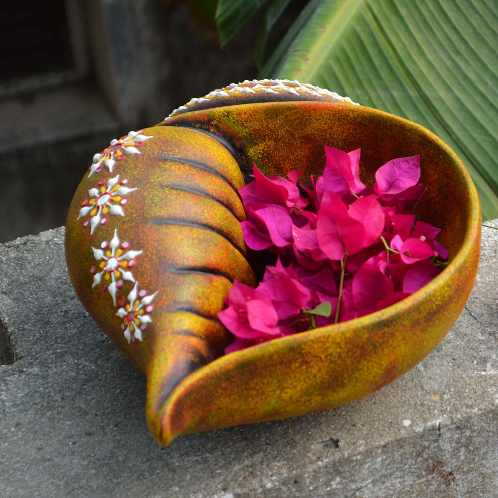 Handcrafted multicolor earthen Sanghu Urli in a conch shell design, adorned with floral accents, filled with pink bougainvillea petals.