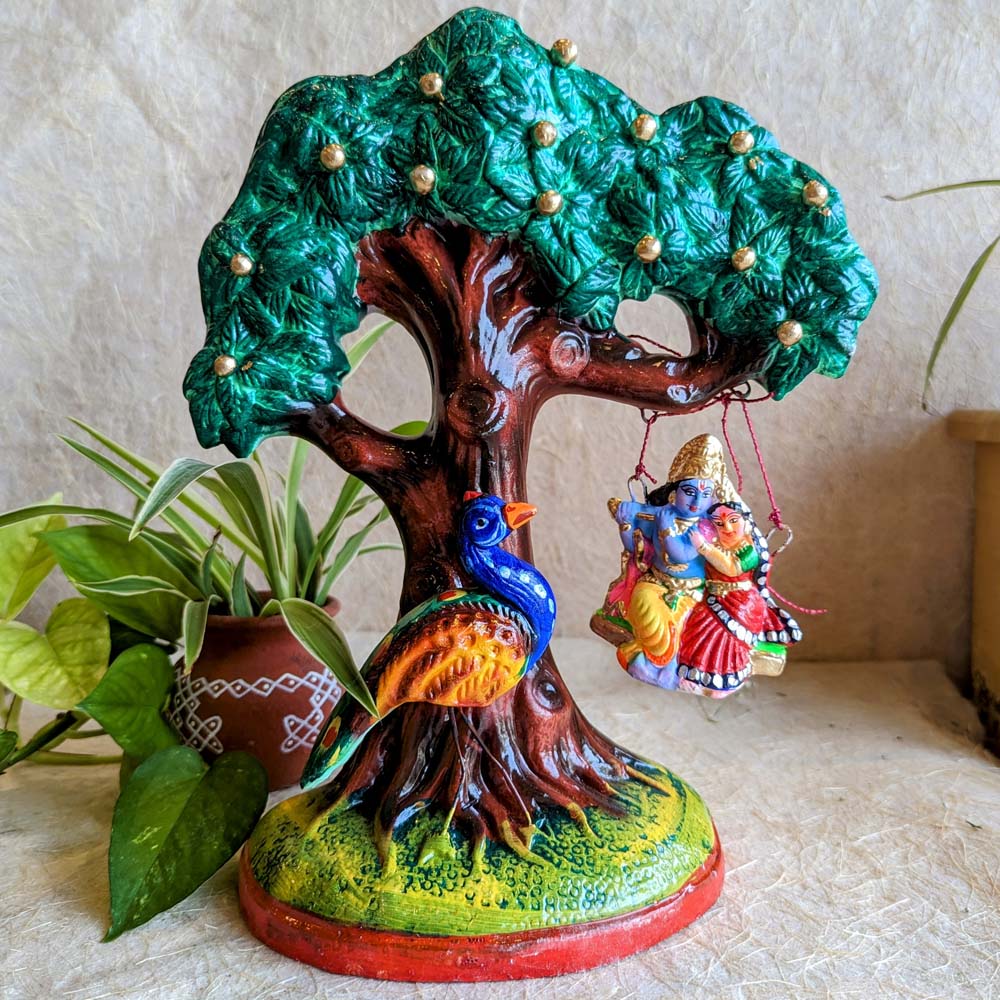 Handcrafted Navarathri Golu Doll featuring Radha Krishna on a jhula under a Kadamba tree with a colorful peacock.