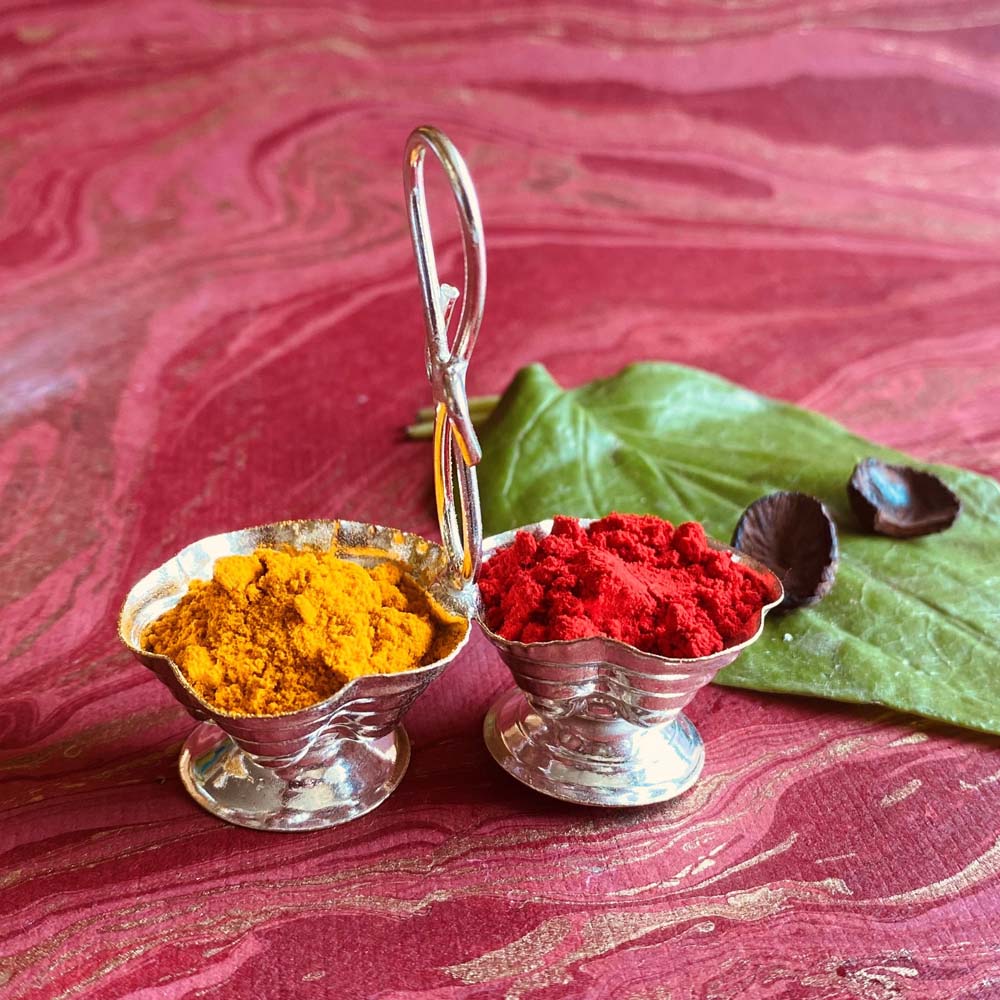Silvery dual haldi kumkum cup with floral design and connecting handle, perfect for pooja rituals and festive decor.