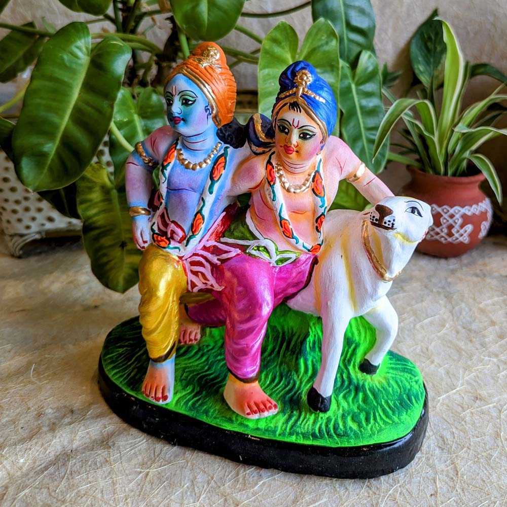 Handcrafted Golu doll depicting Krishna and Balram standing with a cow on a grassy base, beautifully painted in vibrant colors.