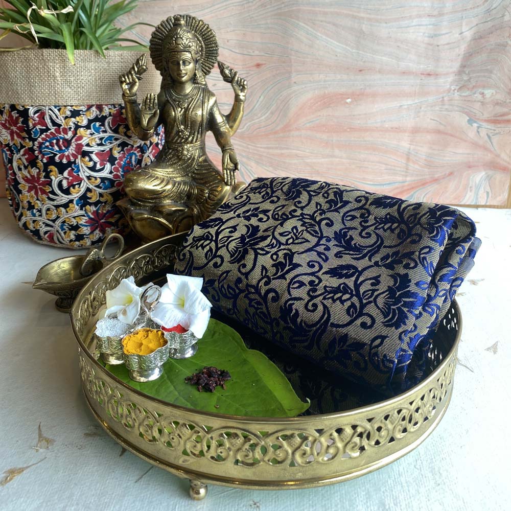 Indian Banaras weave fabric in dark blue with intricate floral patterns displayed alongside a decorative brass tray and a Lakshmi idol.