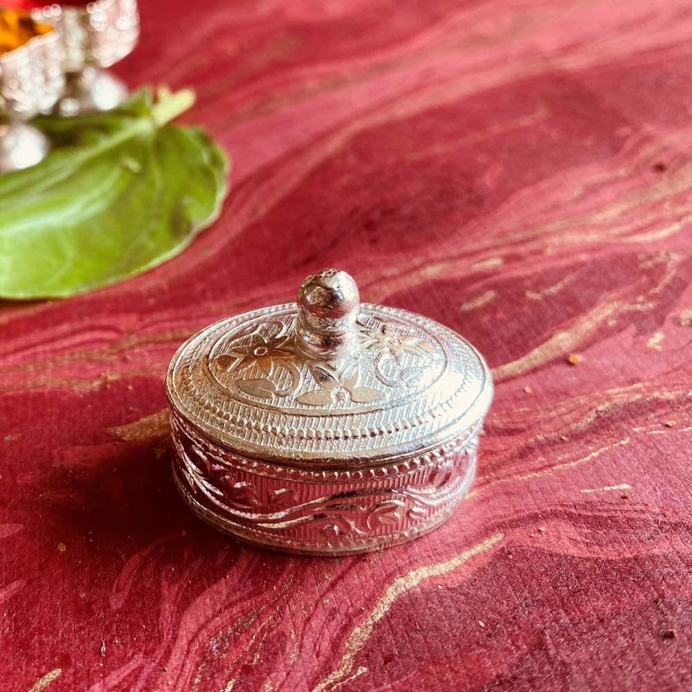 Oval silver kumkum box with intricate floral carvings, perfect for pooja rituals and festive decor.