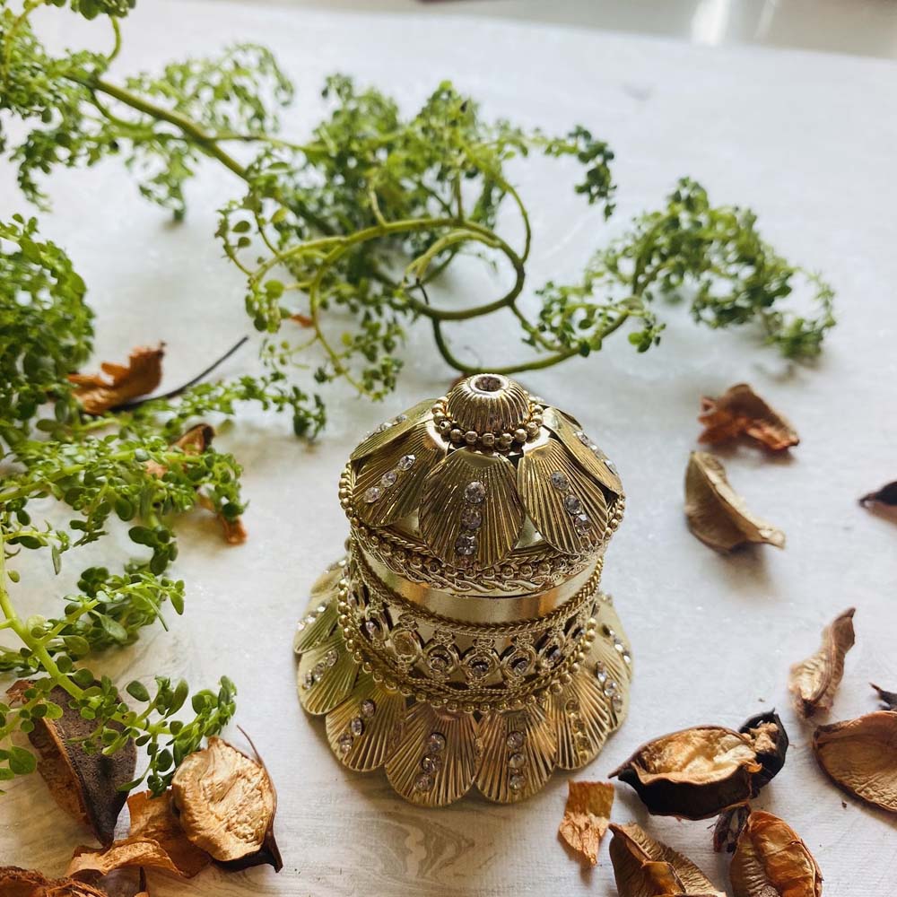 Gold-toned kumkum box with a temple-inspired design and intricate detailing, adorned with sparkling embellishments.