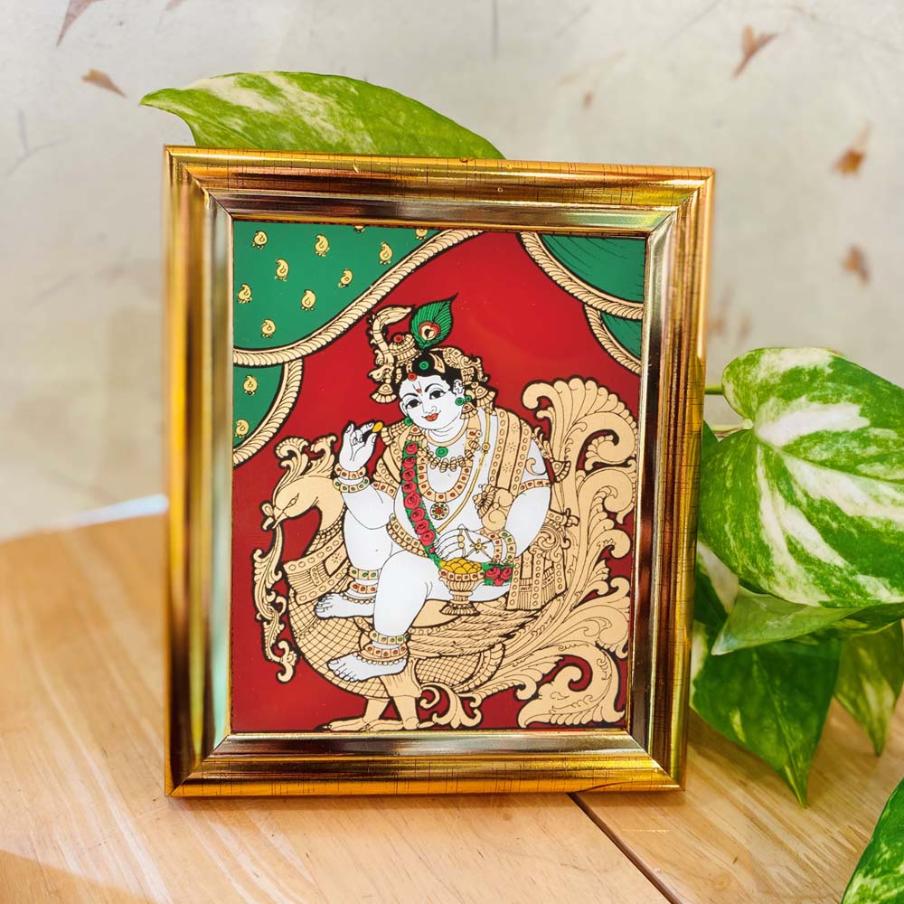 Tanjore-style artwork of Lord Krishna seated on a golden Hamsa, set against a red and green backdrop, framed in a premium gold-colored frame.