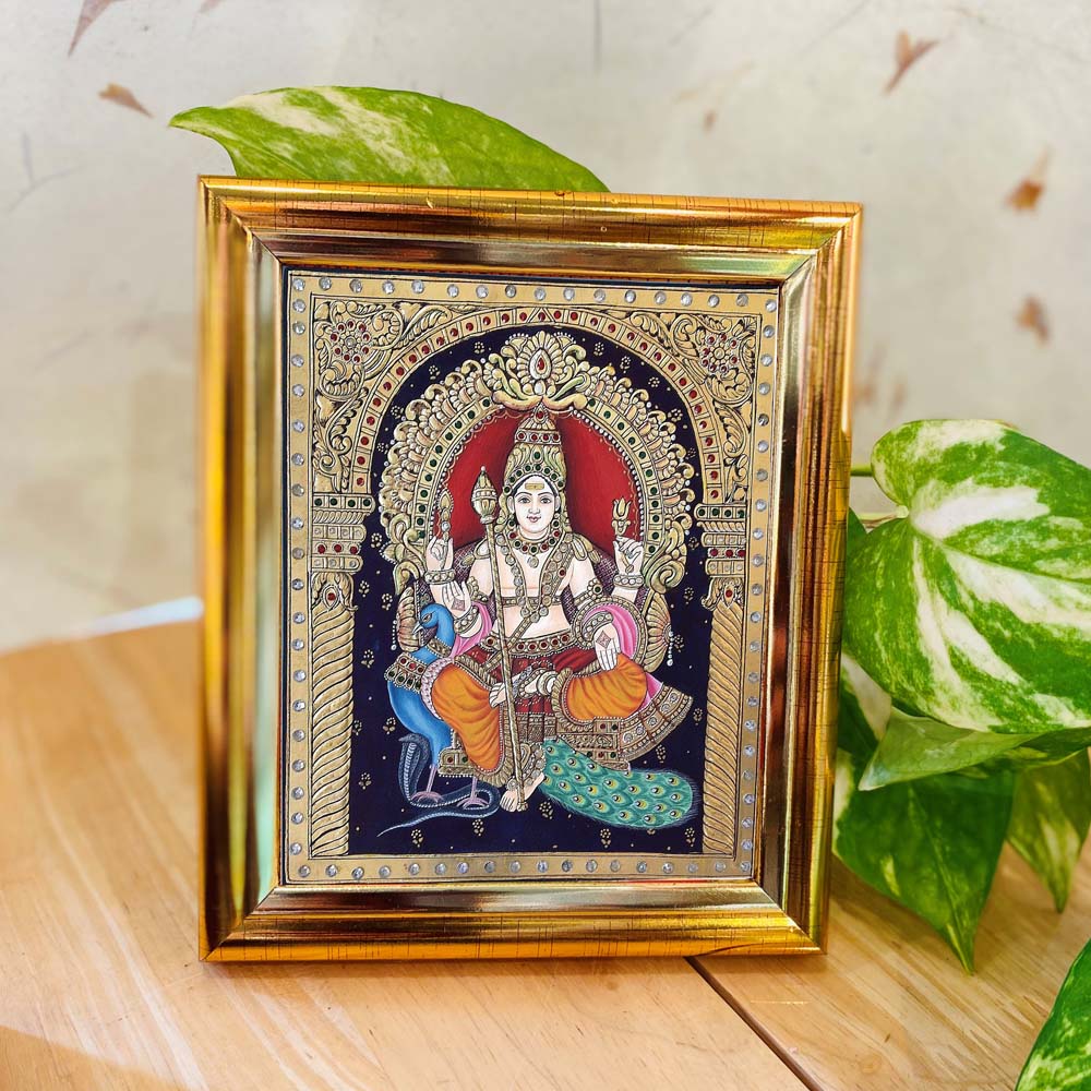 Tanjore-style artwork of Lord Murugan seated on a peacock, set against a black backdrop with intricate detailing and enclosed in a golden frame.