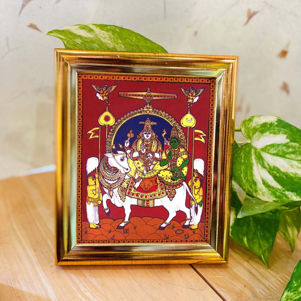 Tanjore-style artwork of Rishabavahana, featuring Lord Shiva and Goddess Parvathi seated on Nandi, set against a maroon backdrop with a golden frame.