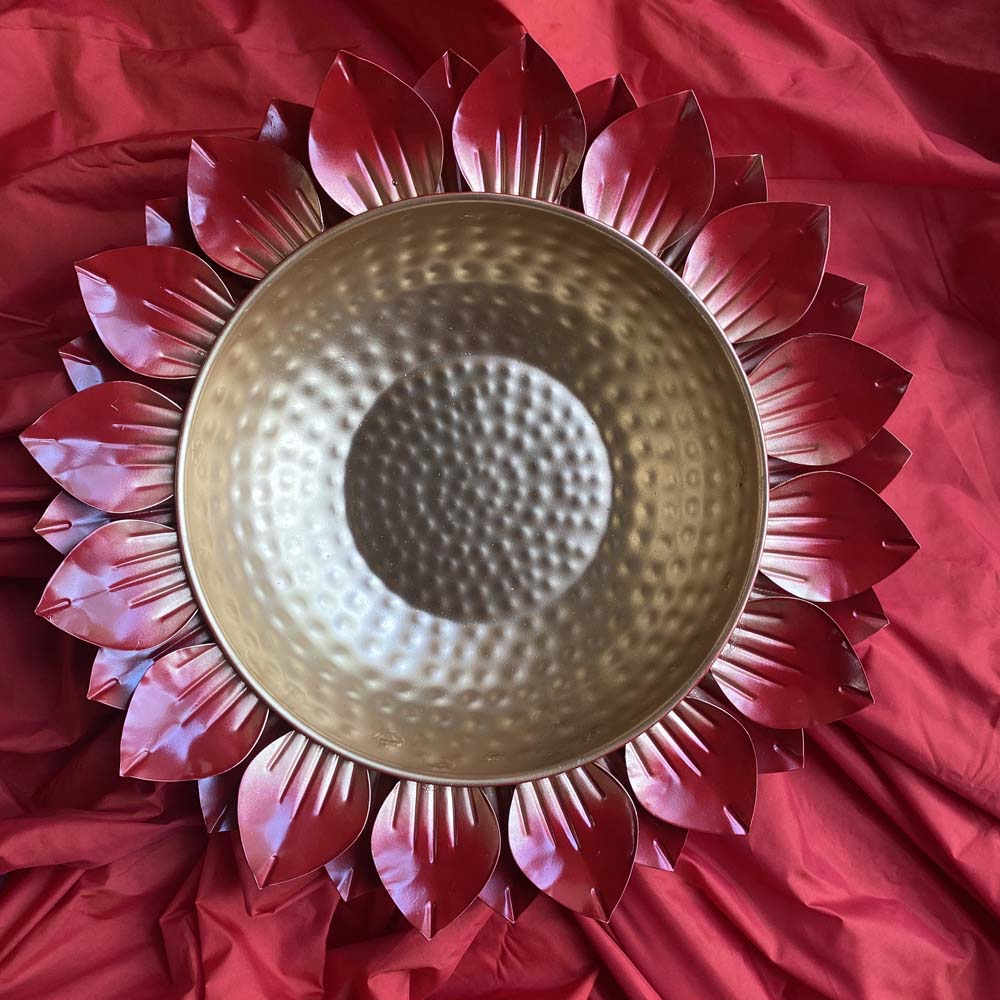 Large decorative urli with a gold hammered metal bowl surrounded by vibrant red lotus petals, placed on a red fabric backdrop.
