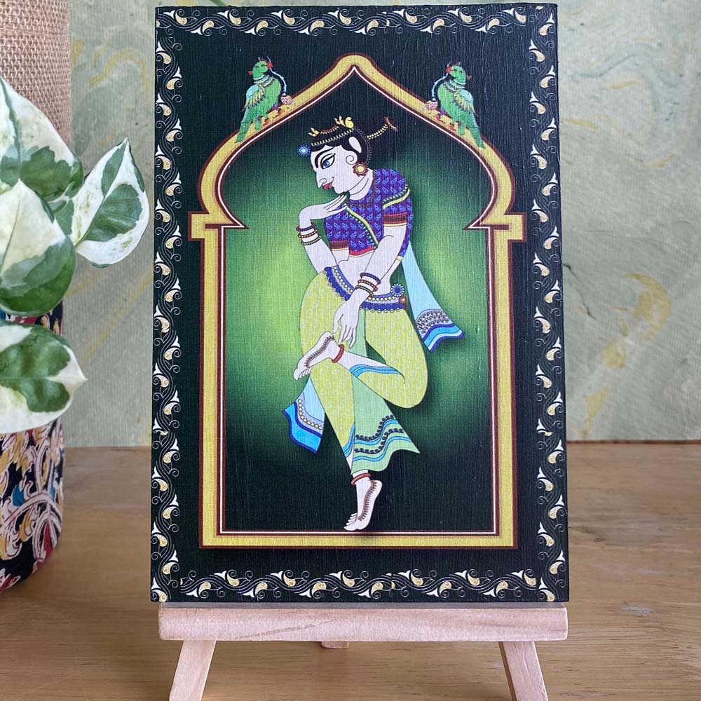 Decorative artwork of a village lady in vibrant blue and green attire, framed by a minaret-style arch with intricate detailing, displayed on a wooden easel.
