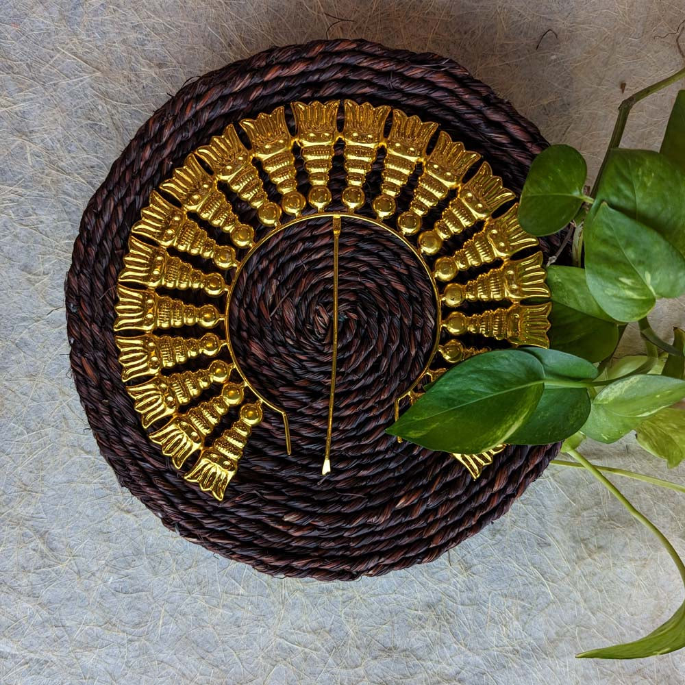 Traditional gold-toned Jada Billai with temple-inspired design, displayed on a woven brown mat with green leaves.
