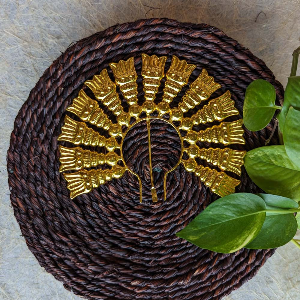 Gold-plated Jada Billai with intricate designs, displayed on a woven brown background with green leaves.