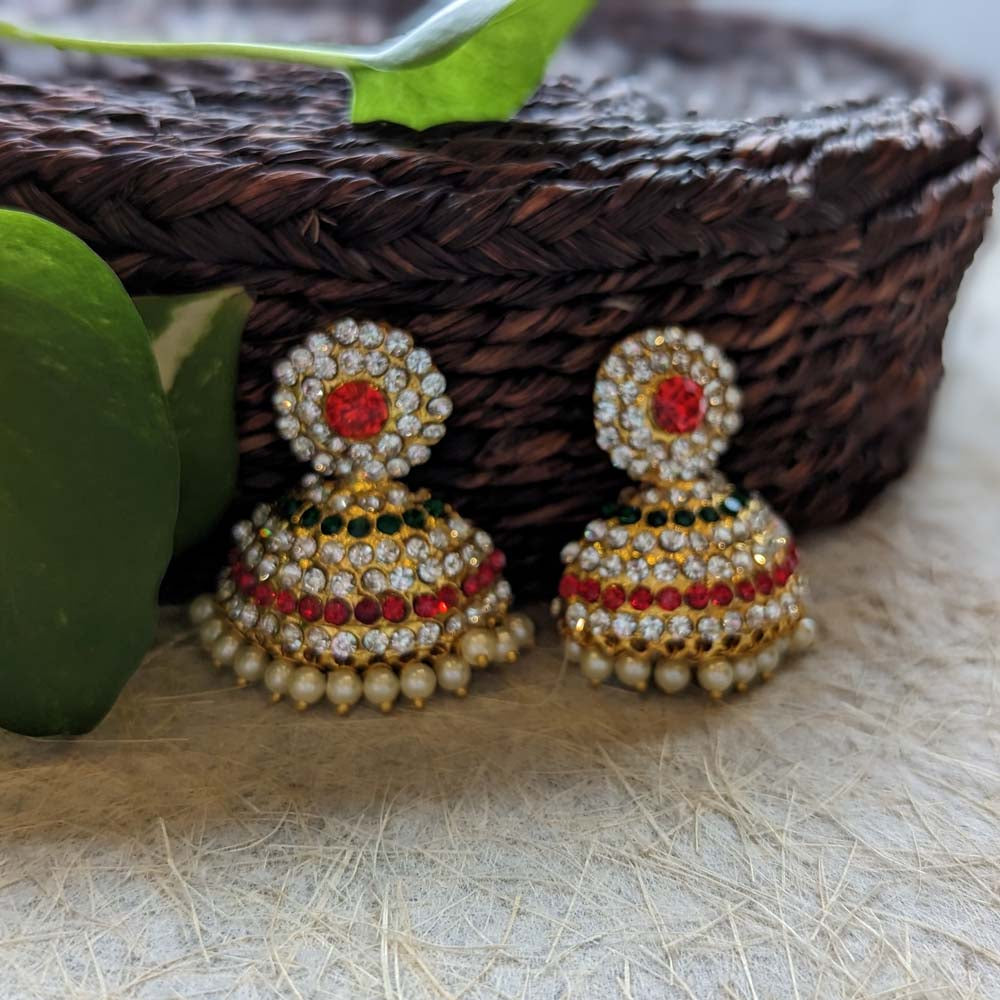 Traditional gold-plated jhumki earrings with red, green, and white stones, and pearl accents, displayed on a woven background.