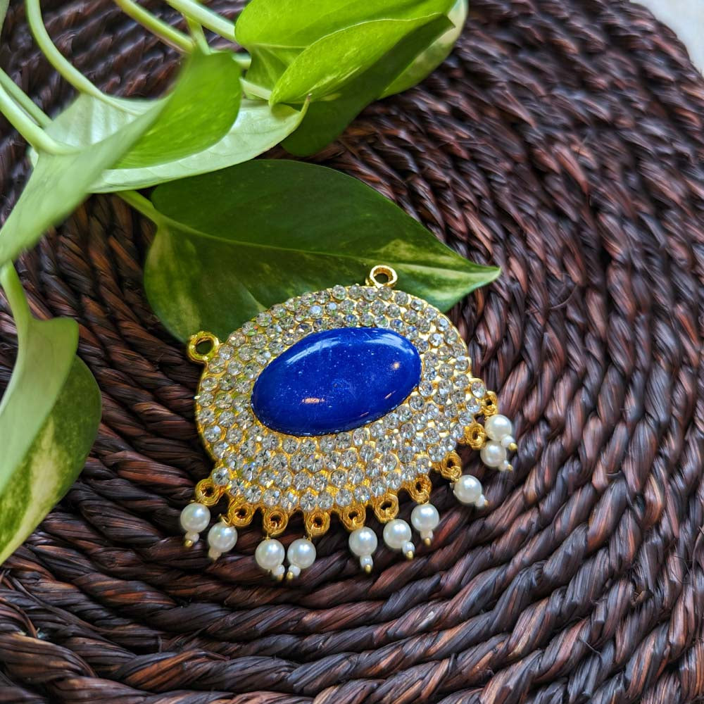 Gold-plated pendant with a large blue center stone, crystal detailing, and pearl accents on a woven brown background.