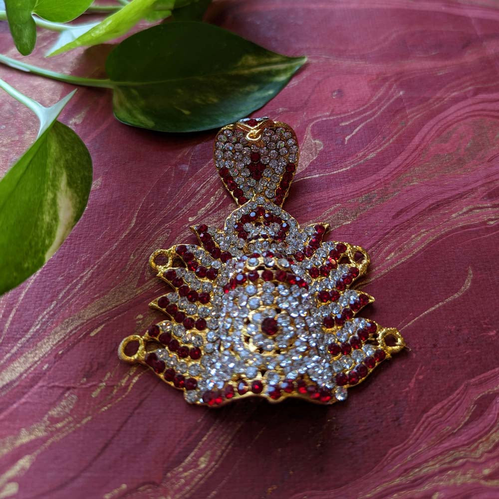 Gold-tone crown pendant adorned with ruby-red and crystal stones on a maroon background with green leaves.