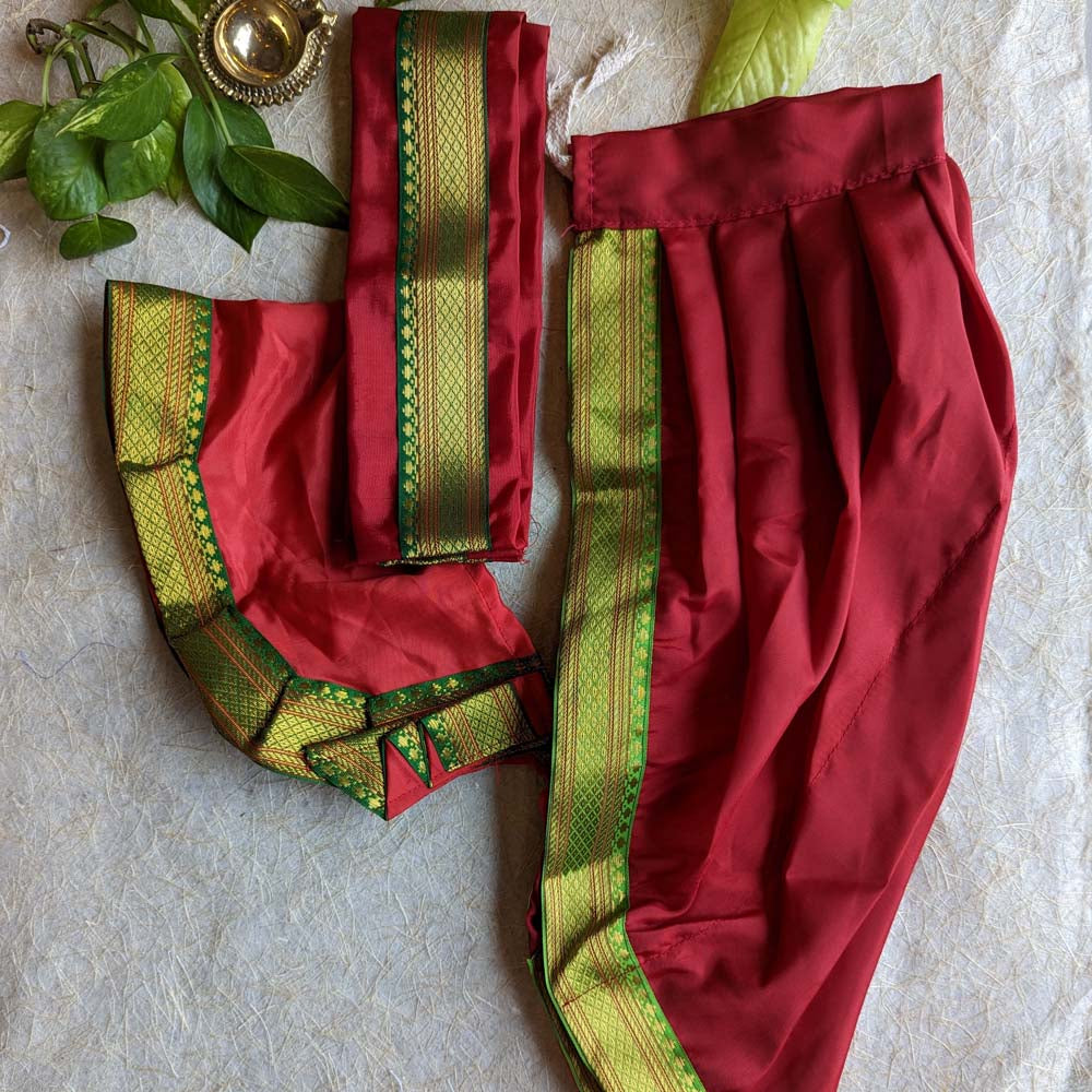 Traditional orange dhoti and angavastram set with green and gold zari borders, displayed on a textured background with leafy accents.