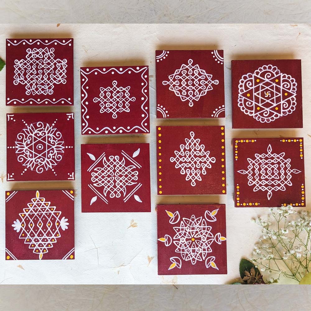 Rich maroon wooden manai set featuring traditional hand-painted kolam designs in white with yellow accents, set against a light decorative background.