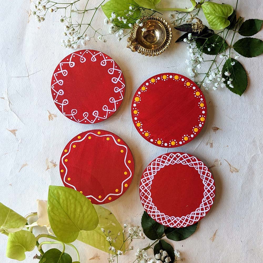 Handcrafted red round wooden coasters with intricate white and yellow border designs, set against a natural decorative background with floral accents.