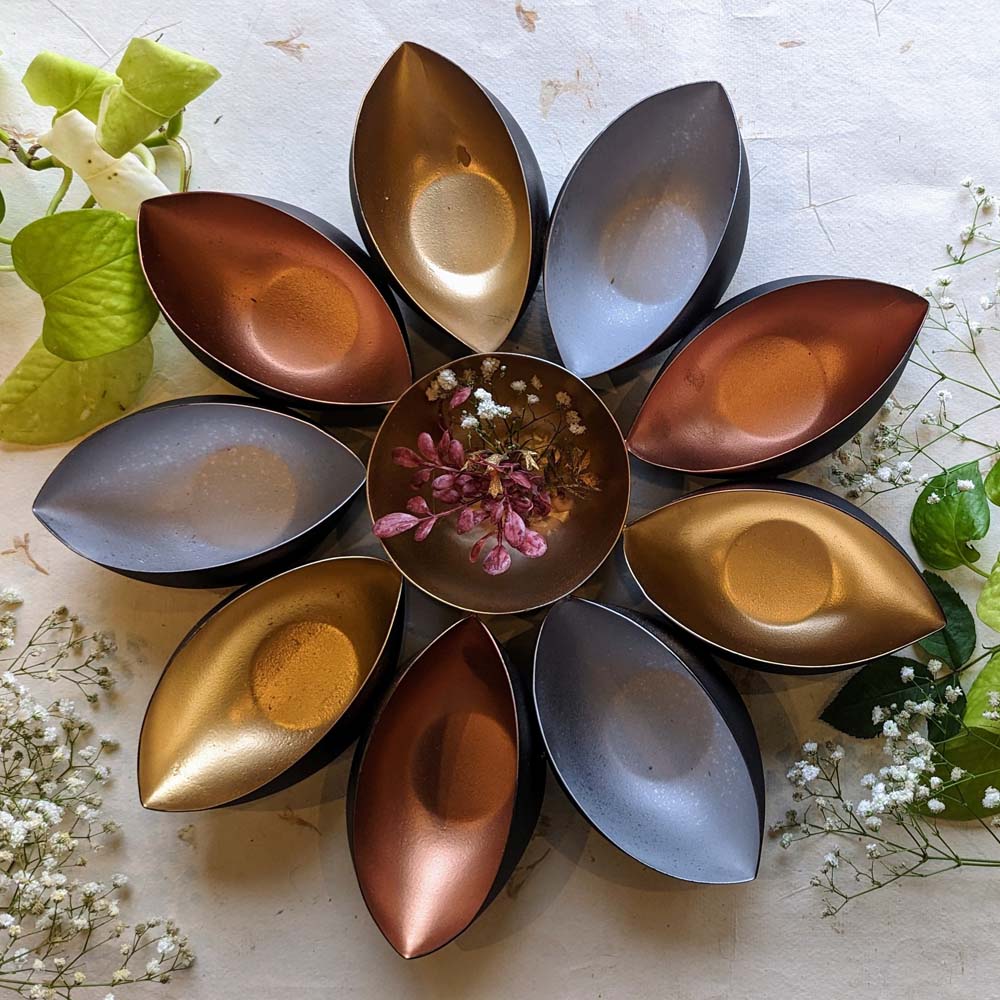 Handcrafted tricolor metal urli bowl with gold, bronze, and silver petals surrounding a central bowl, adorned with flowers.