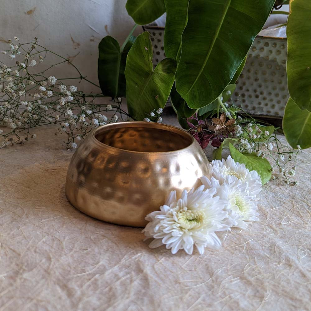 Handcrafted brass bowl planter with a hammered design, adorned with white flowers and surrounded by greenery.