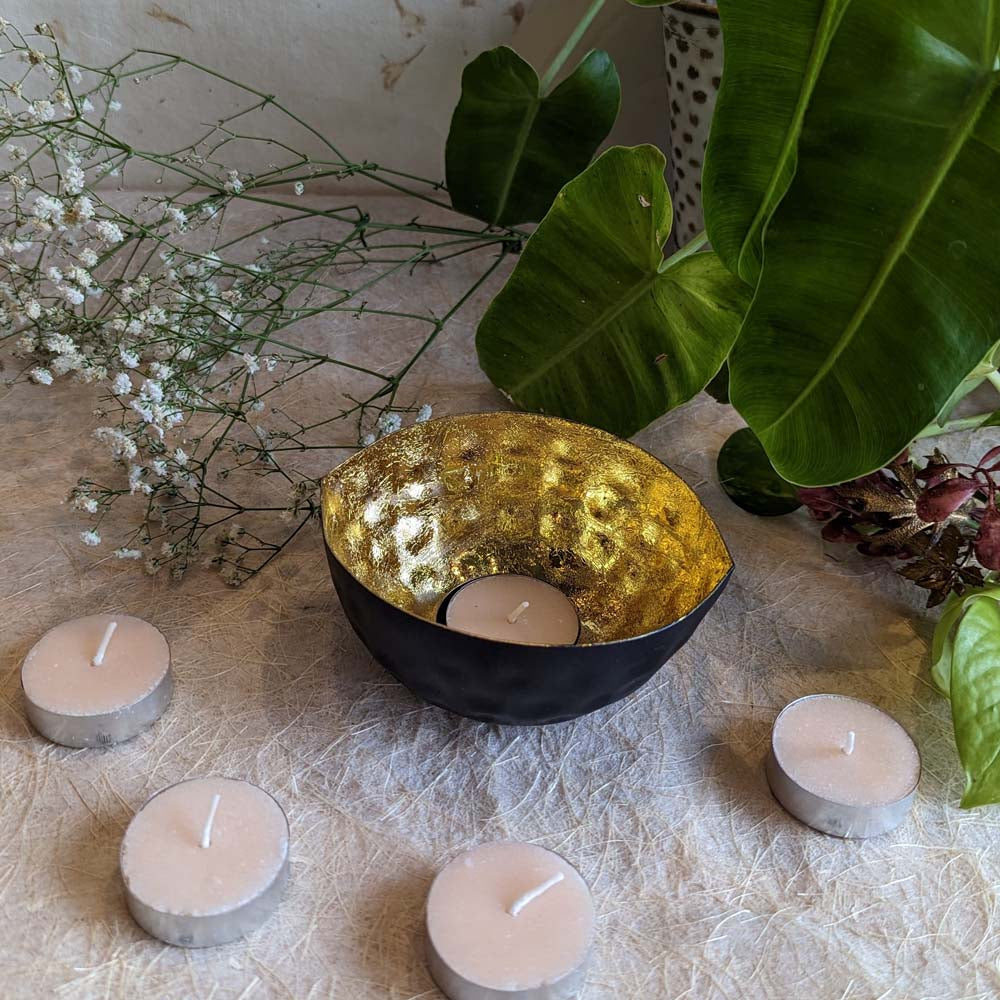 Handcrafted eye-shaped tealight holder with a hammered gold interior and matte black exterior, surrounded by tealights and natural greenery.