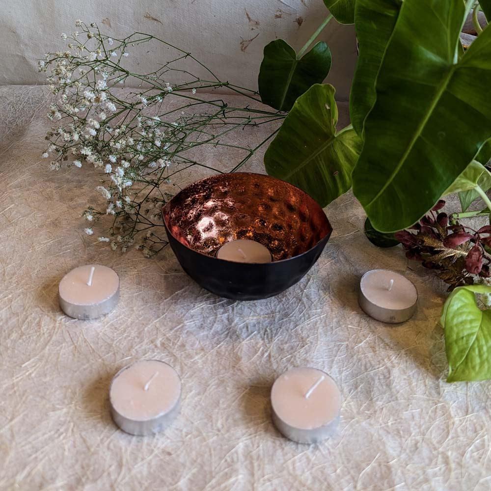 Handcrafted eye-shaped tealight holder with hammered copper interior and black matte exterior surrounded by tealights and natural decor.