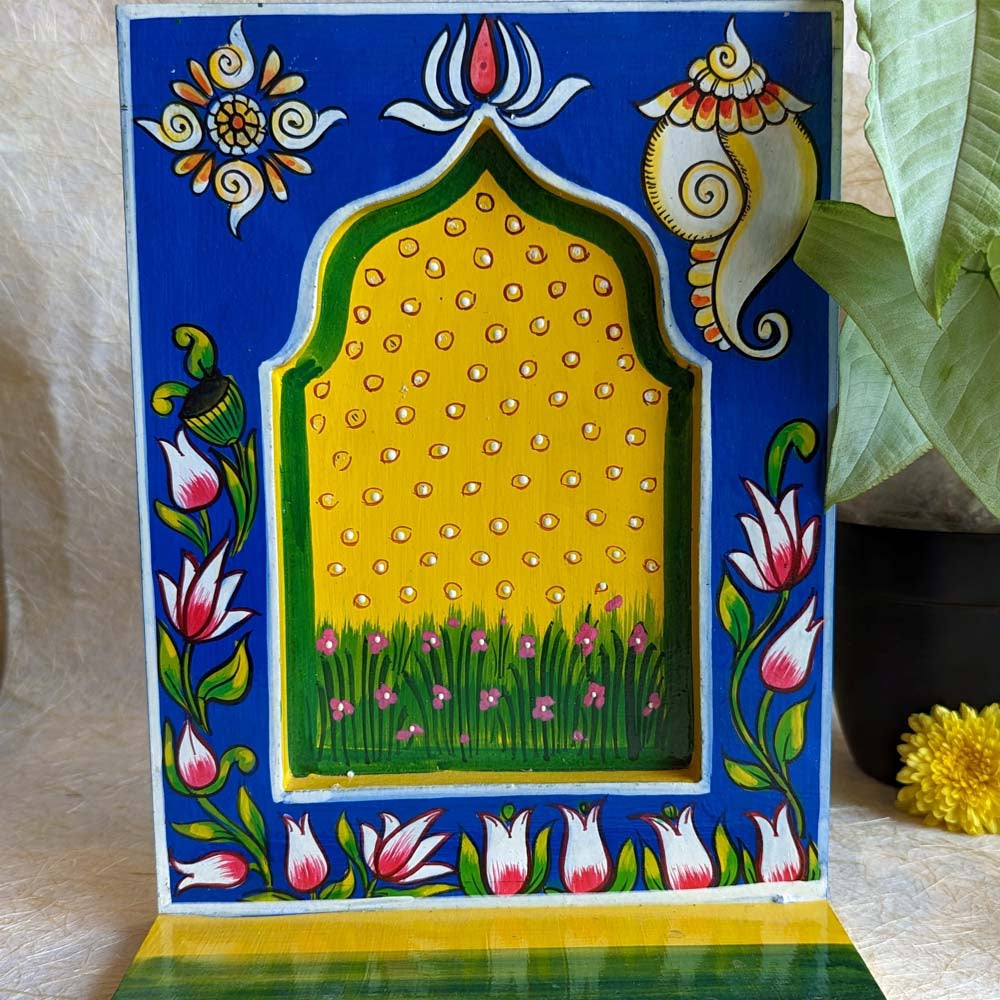 Hand-painted wooden wall shelf with yellow and blue tones, featuring conch shell, lotus motifs, and floral patterns with an arched design.