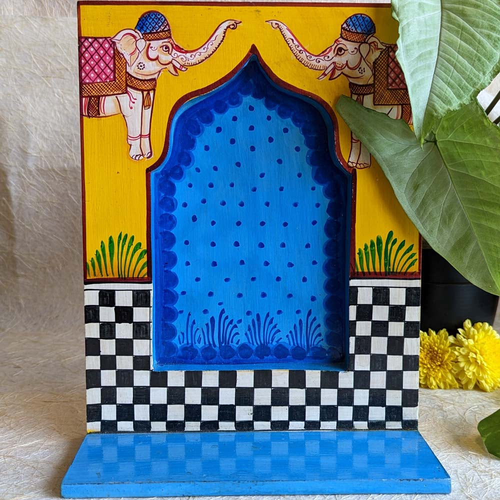 Hand-painted wooden wall shelf with yellow and blue tones, featuring elephant motifs, black-and-white checkered patterns, and a traditional arched design.