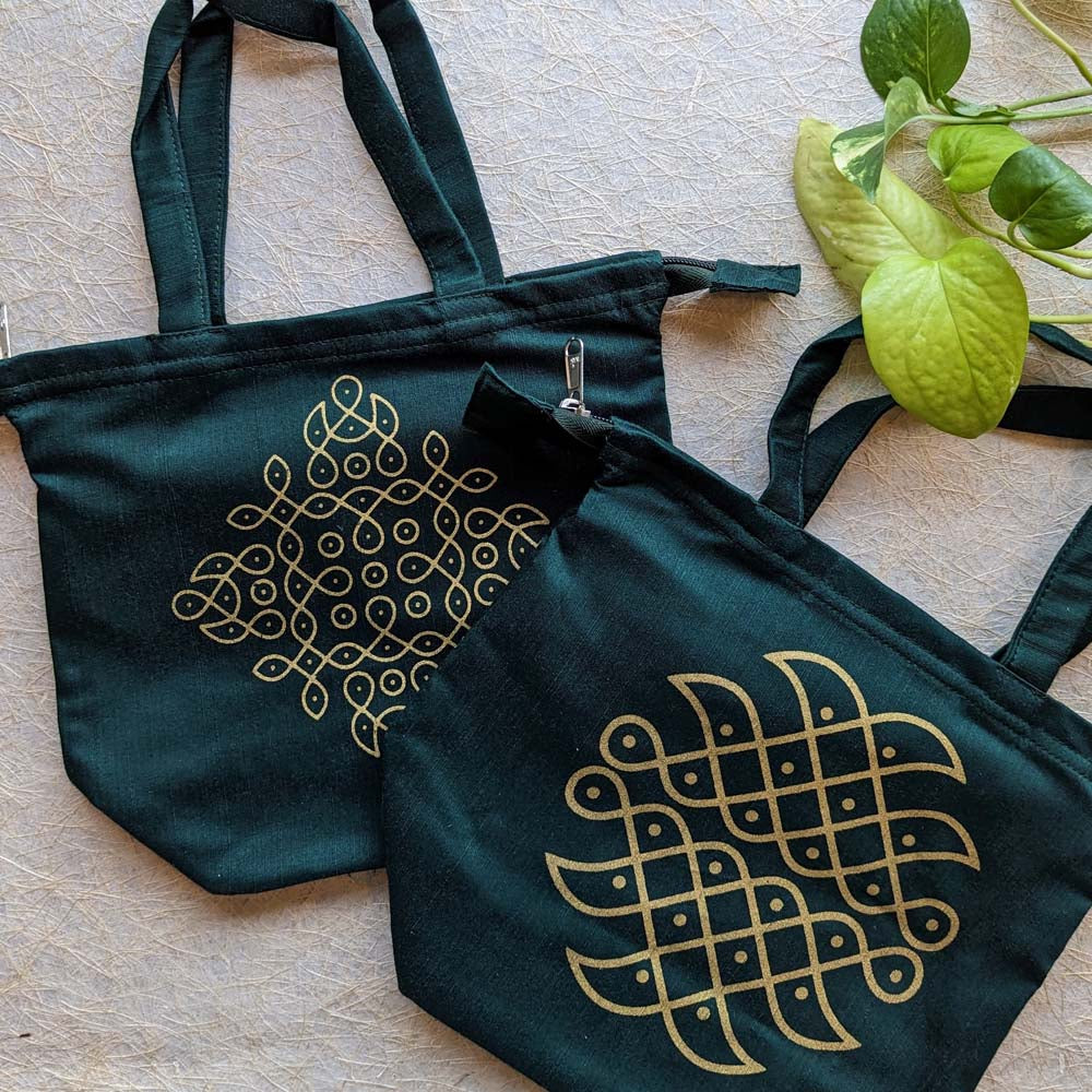 Green cotton tote bags featuring golden kolam designs, displayed on a textured background with green leaves.
