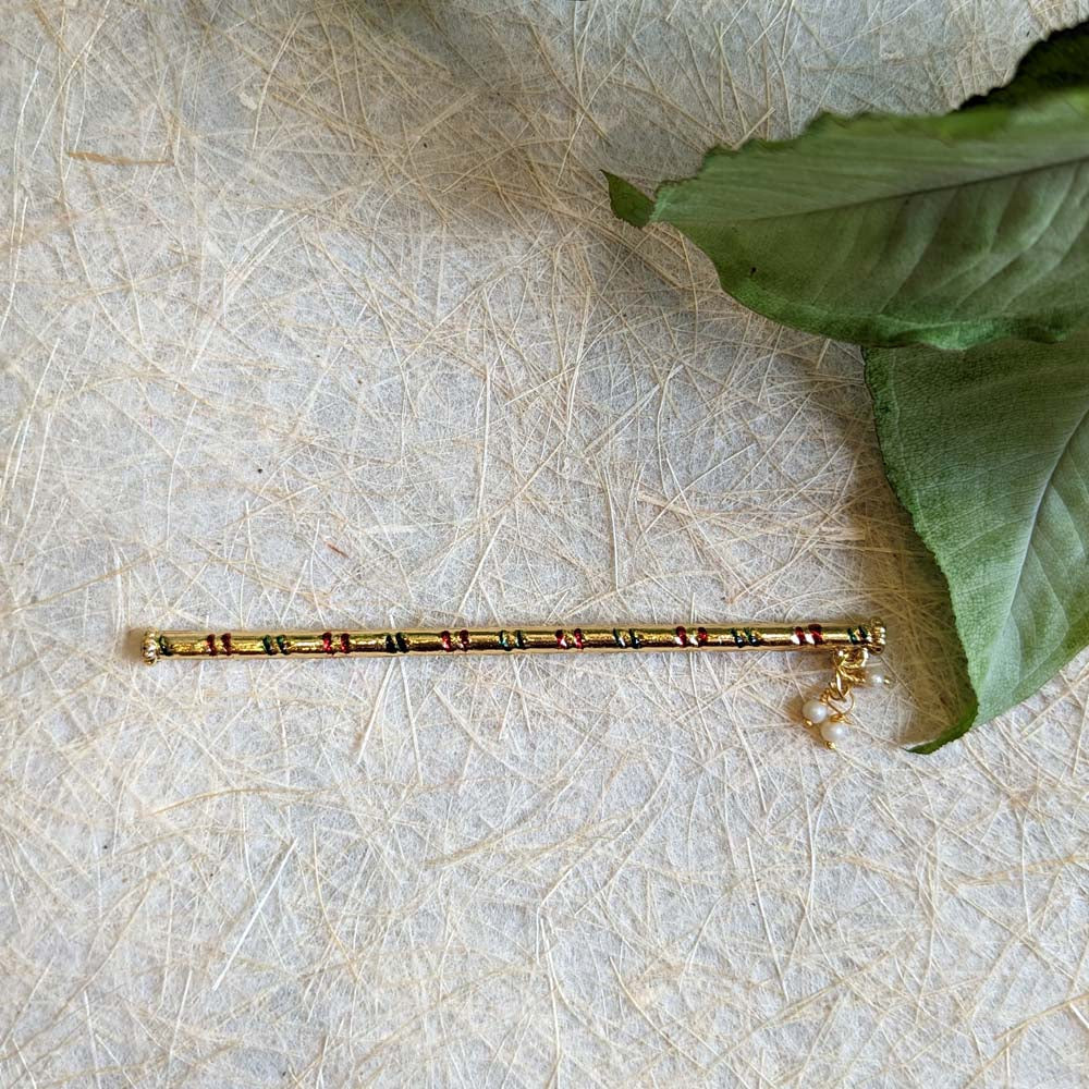 Krishna’s plain golden flute with red and green embellishments and pearl detailing.